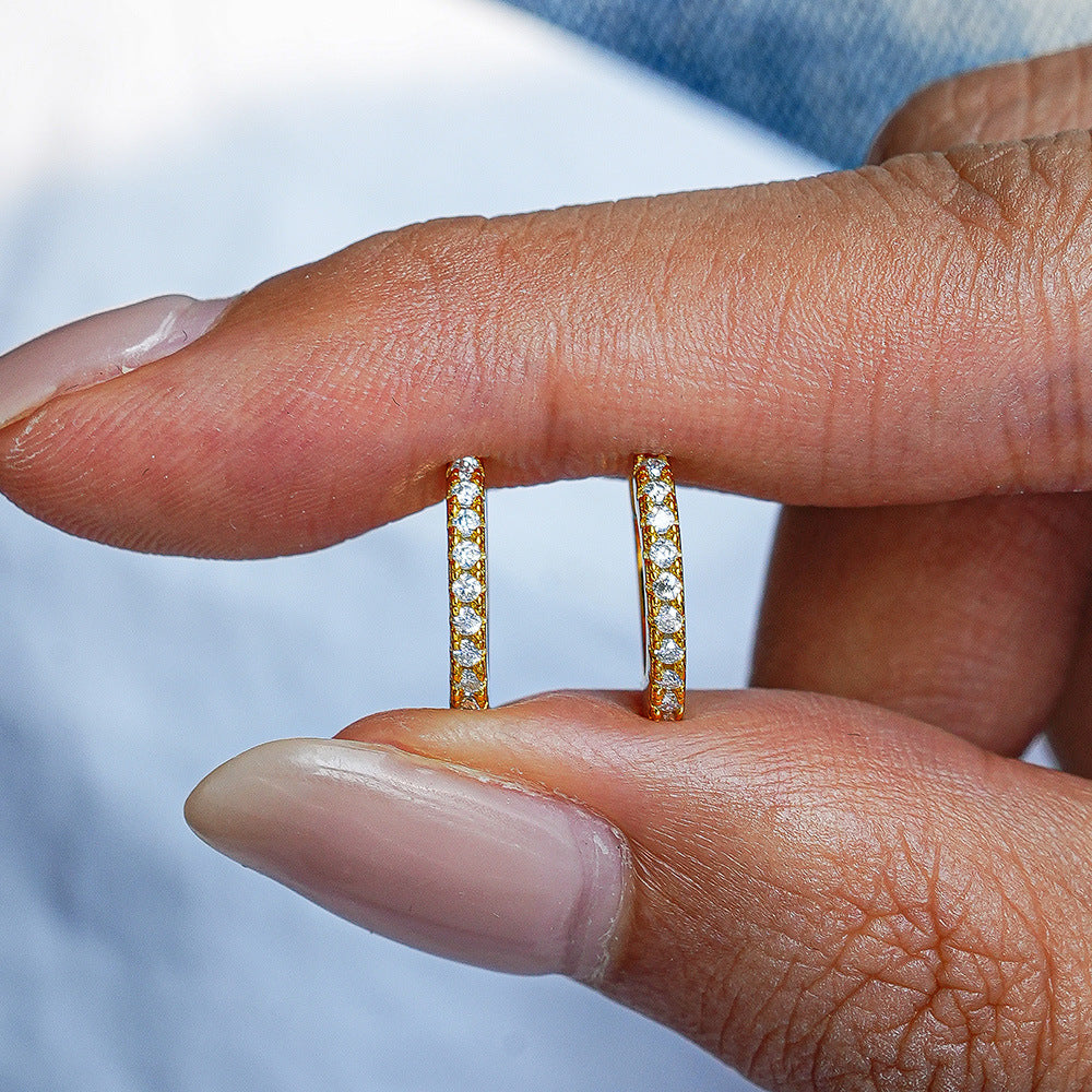 Gold hoop earrings held between fingers against a blurred background
