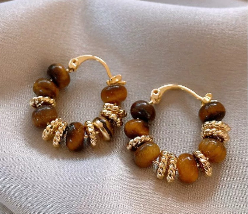Pair of hoop earrings with brown beads and gold accents on a beige fabric background  from nested wisdom