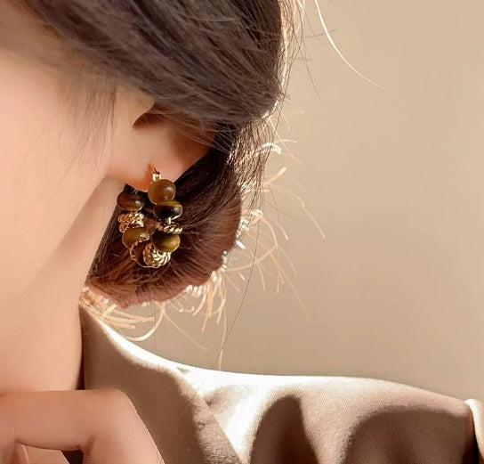 Close-up of an ear wearing a gold and green beaded earring with a blurred background  from nested wisdom
