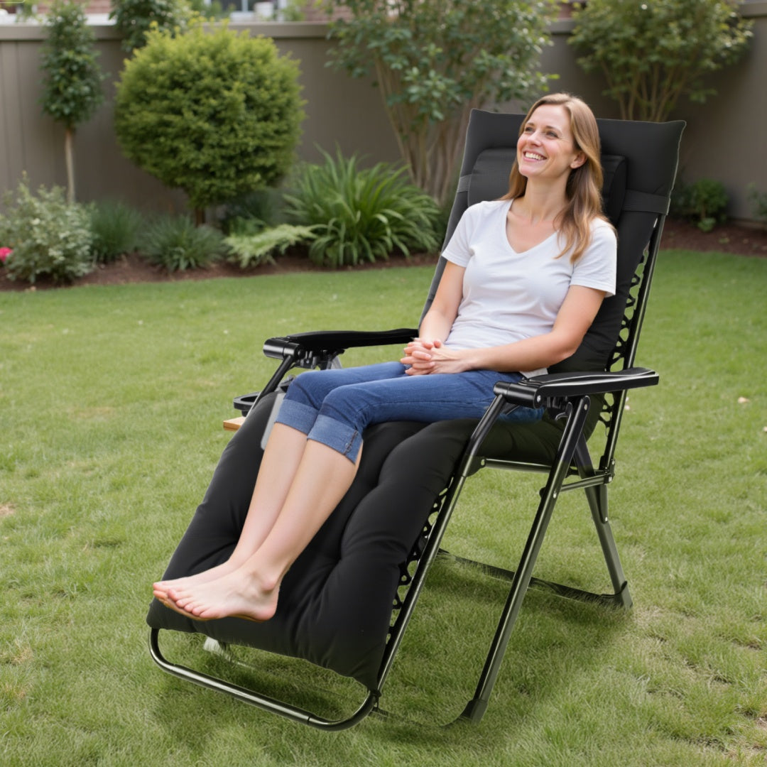 Woman sitting in a black reclining chair on a grassy area with plants in the background