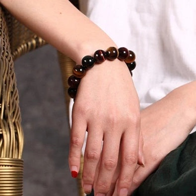 Close-up of a hand wearing a dark eye of the tiger beaded bracelet against a neutral background