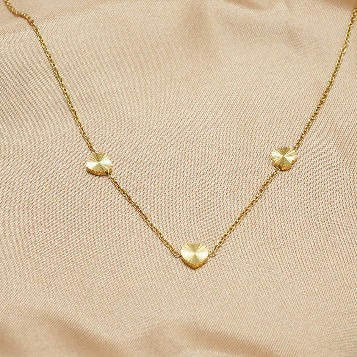 Gold necklace with heart-shaped pendants on a beige fabric background