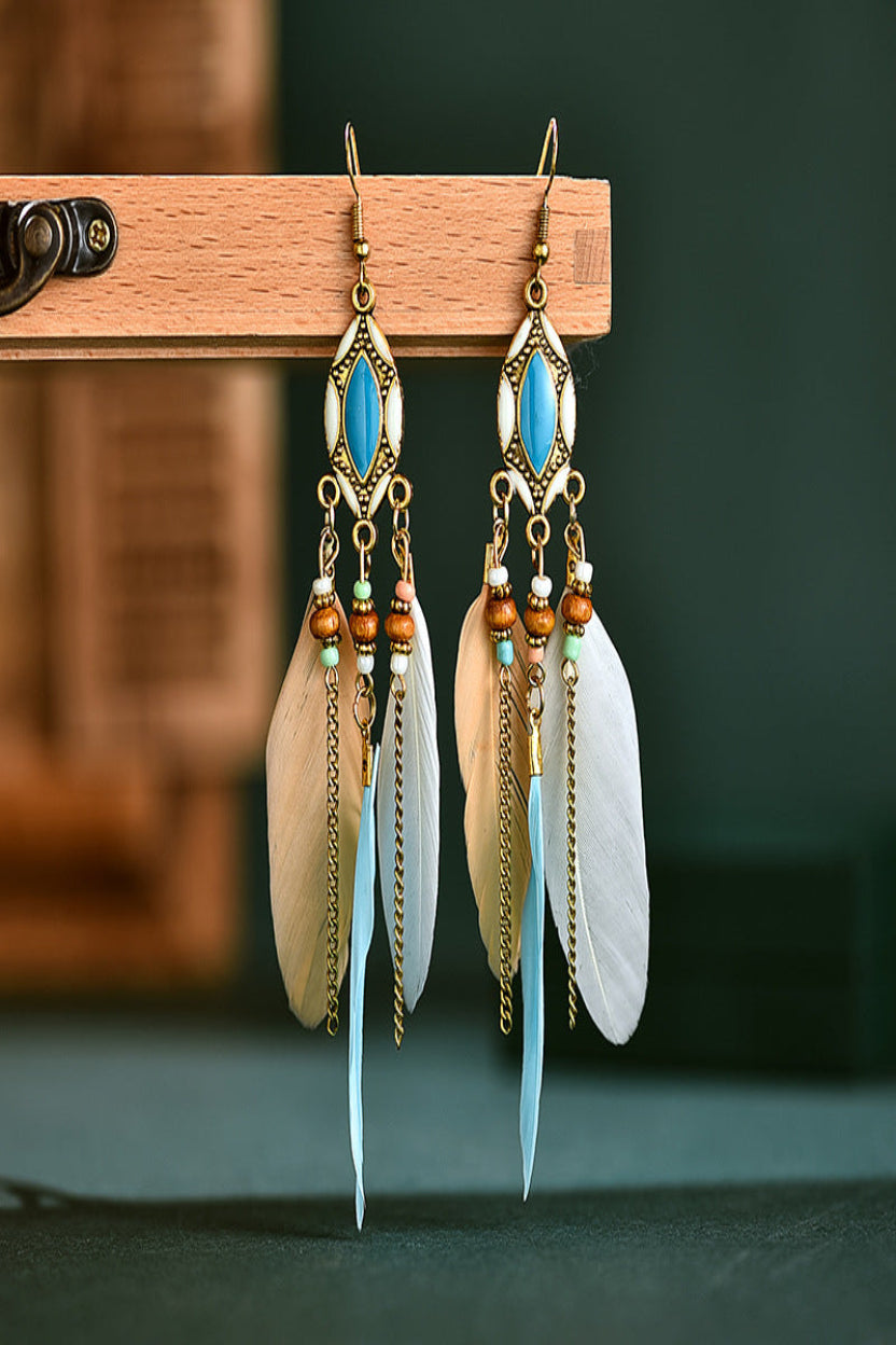 Feather earrings with blue and gold accents on a wooden stand against a dark background from Nested Wisdom