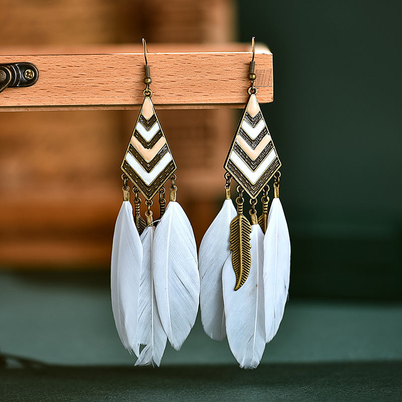 Pair of feather earrings with gold accents on a wooden stand.