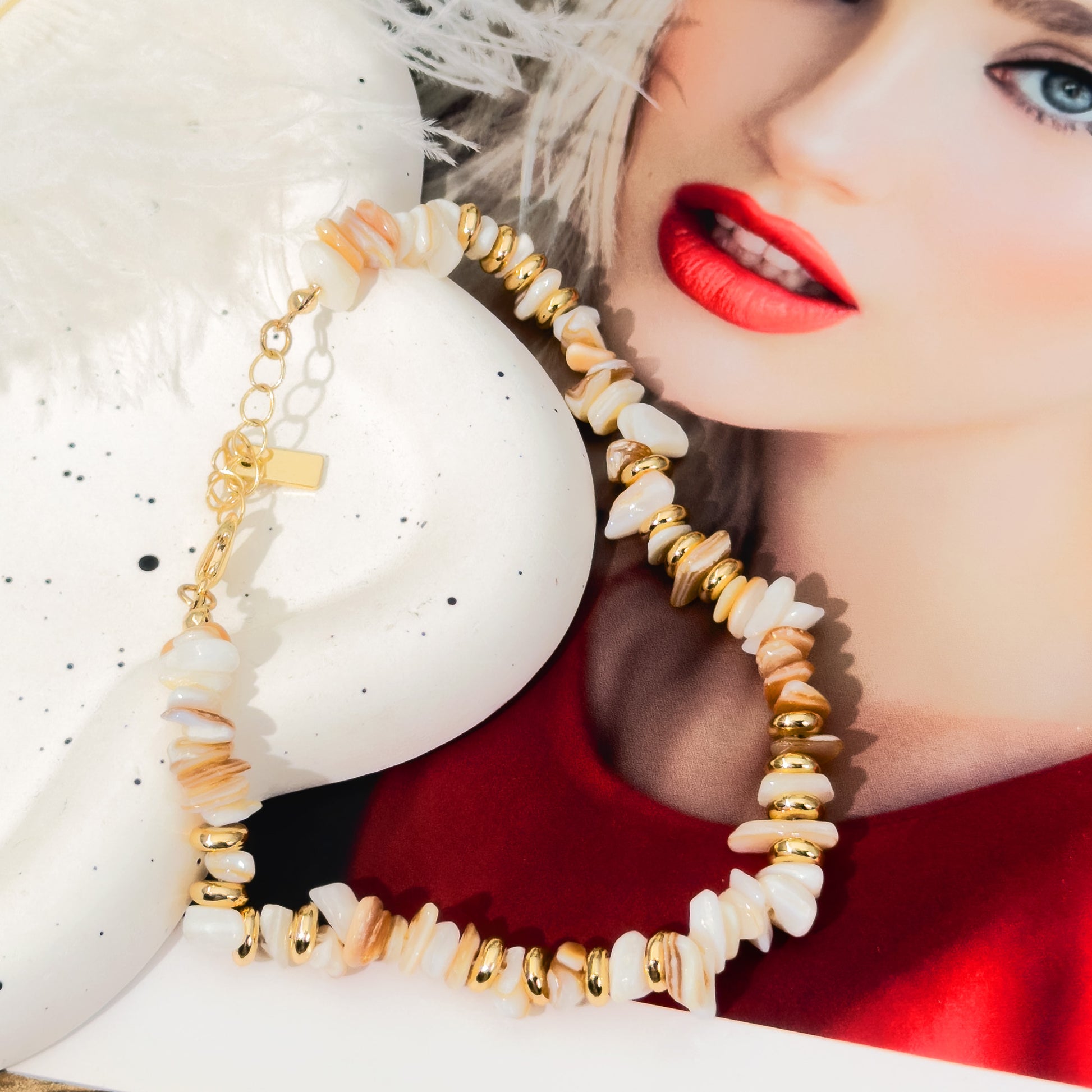 Close-up of a woman wearing gold and beige beaded earrings with a white shell background.