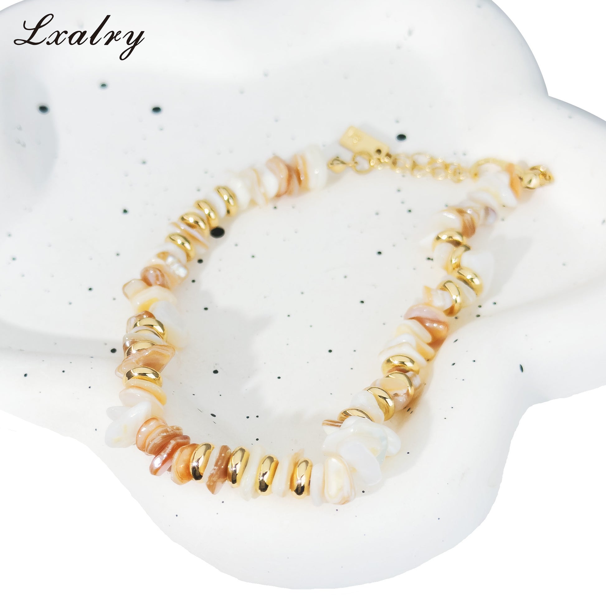 Bracelet with gold and beige beads on a white speckled surface, branded 'Lxalry'.