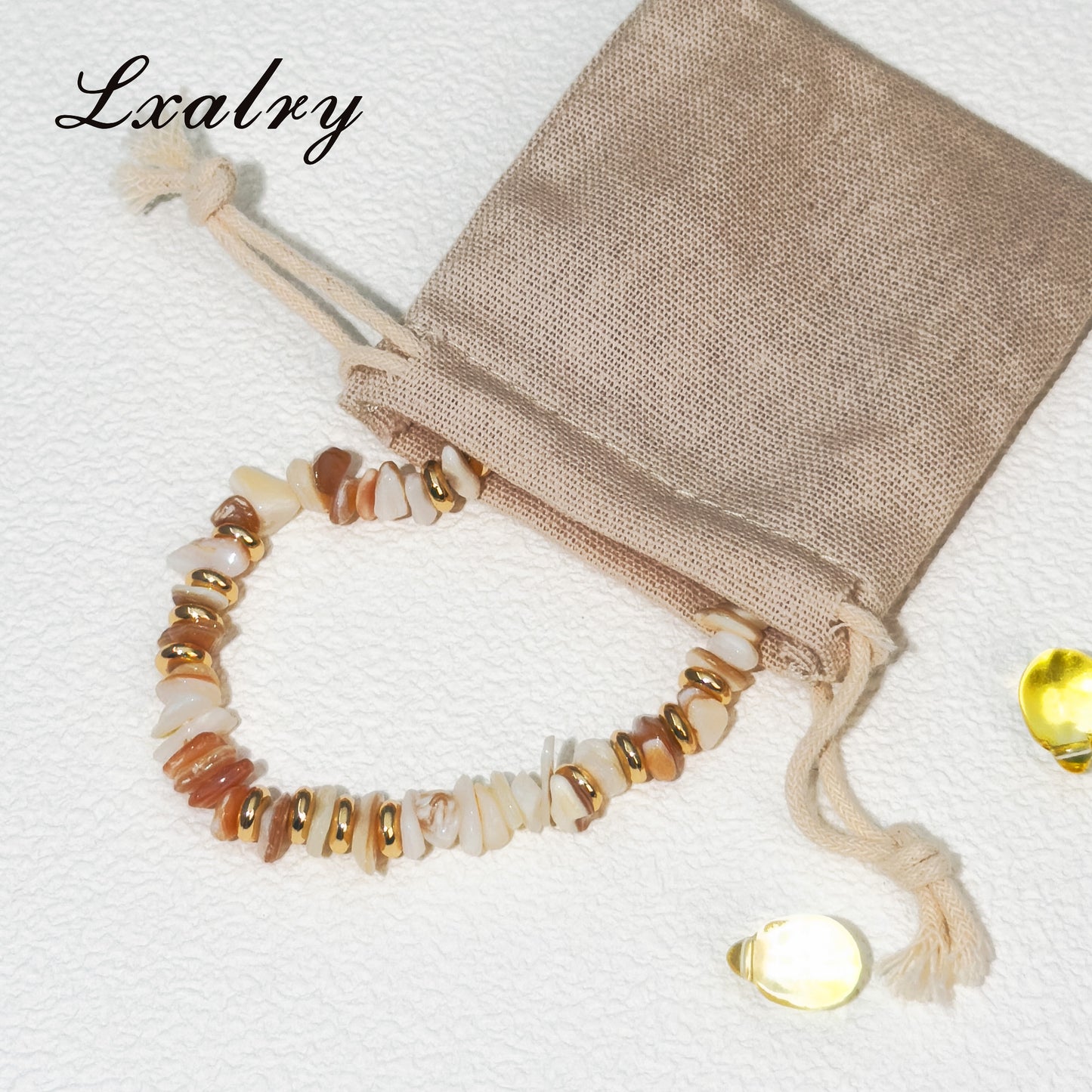 Beaded bracelet with gold accents on a beige drawstring bag, branded 'Lxalry'.