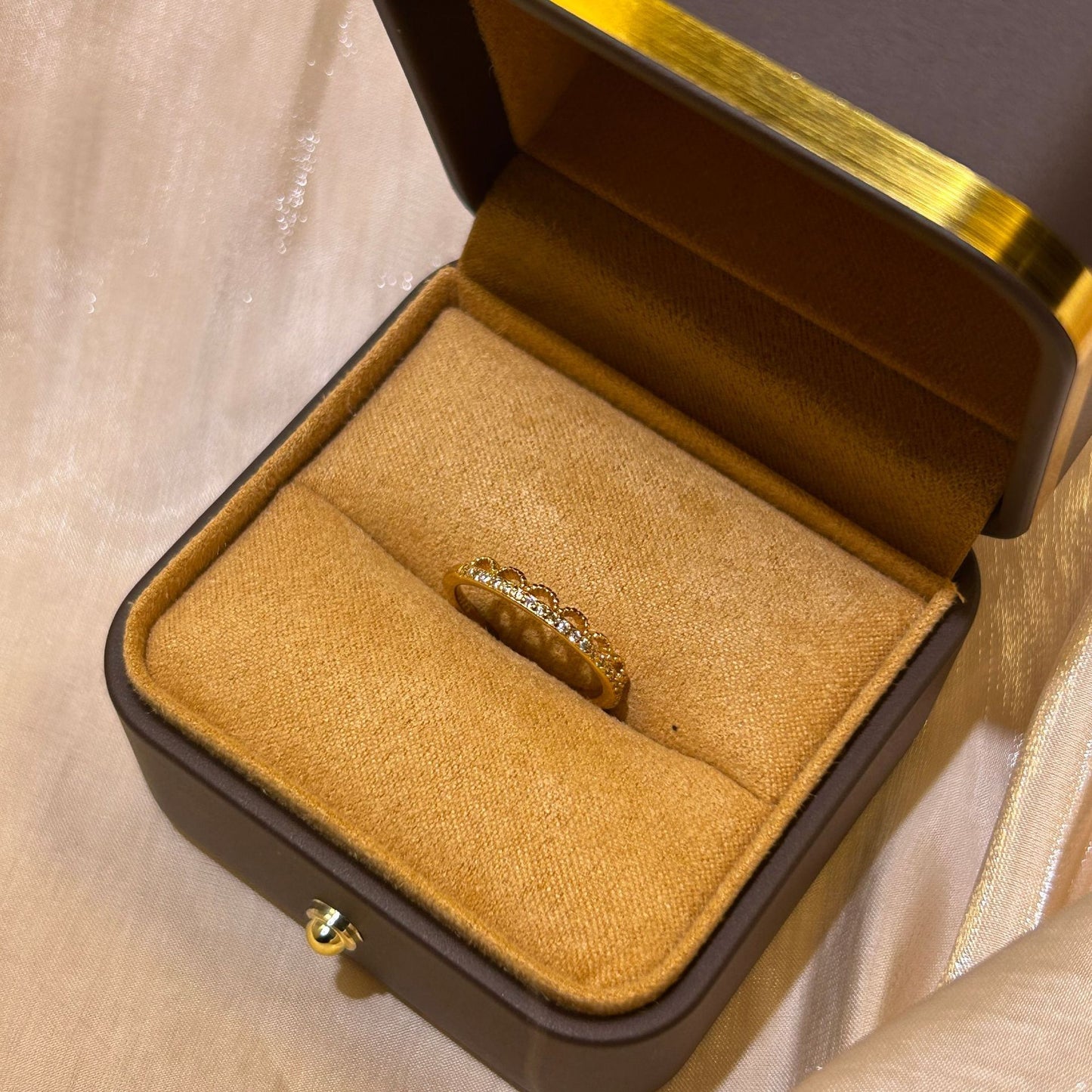Gold ring in a brown jewelry box on a beige fabric background