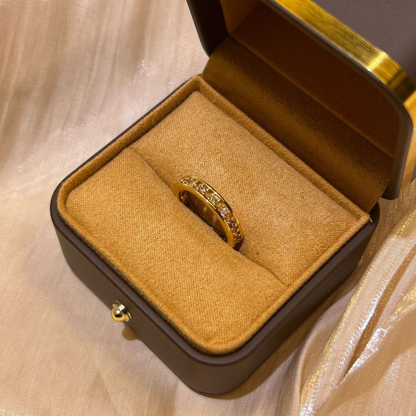 Gold ring with diamonds in a brown jewelry box on a beige fabric background