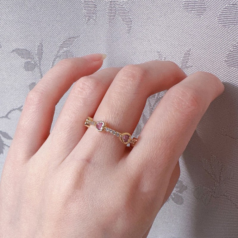 Hand wearing a ring with pink gemstones on a textured gray background