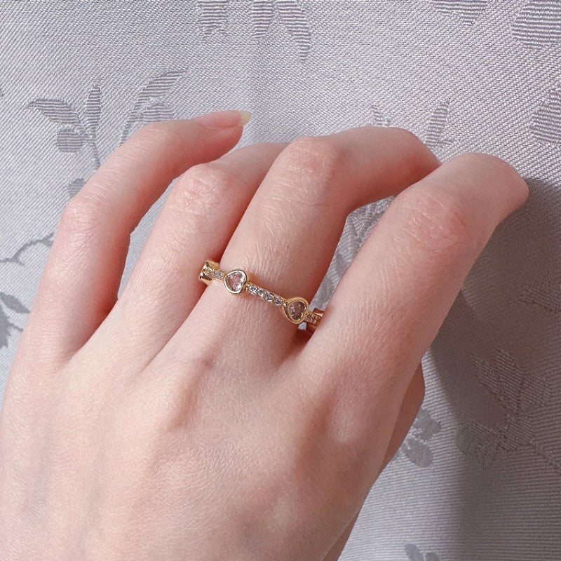 Hand wearing a rose gold ring with small diamonds on a light gray background