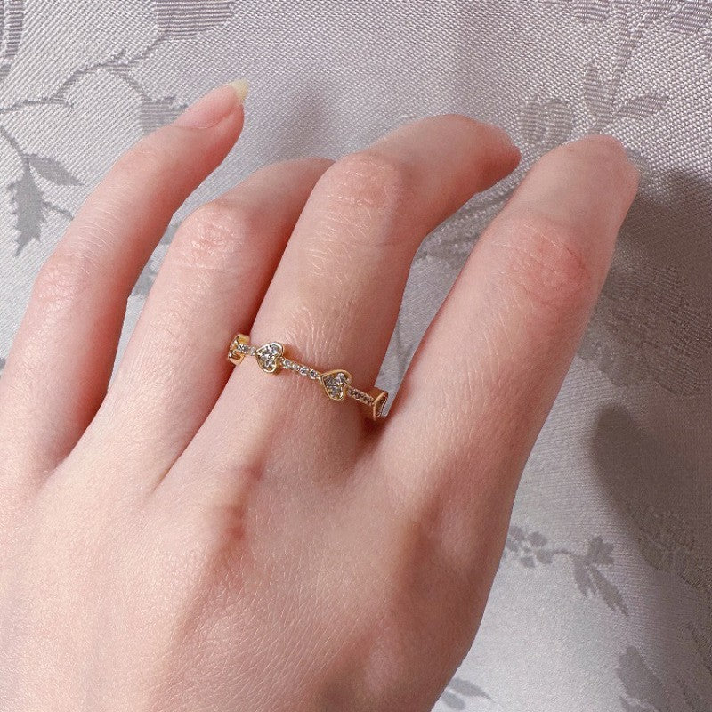 Gold ring with heart designs on a hand against a floral fabric background