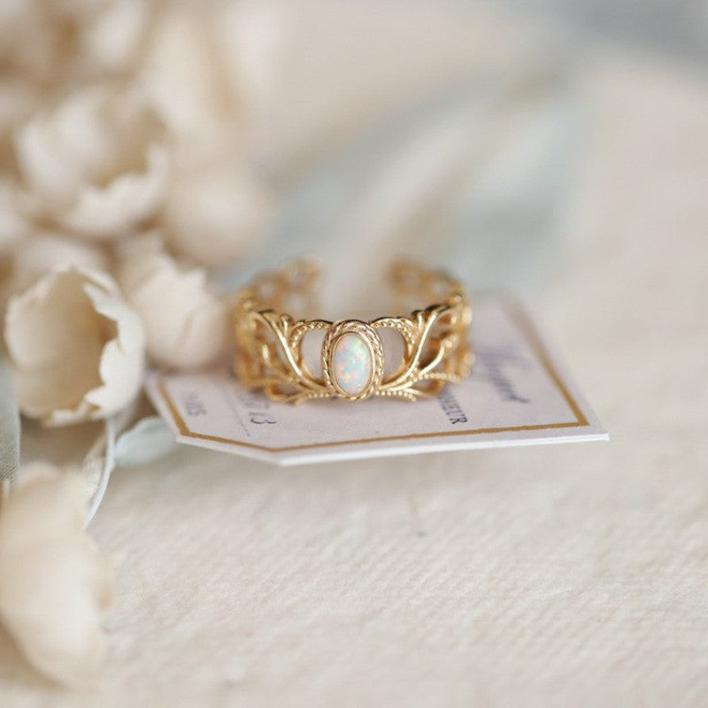 Gold ring with a stone on a white card with text, against a blurred floral background