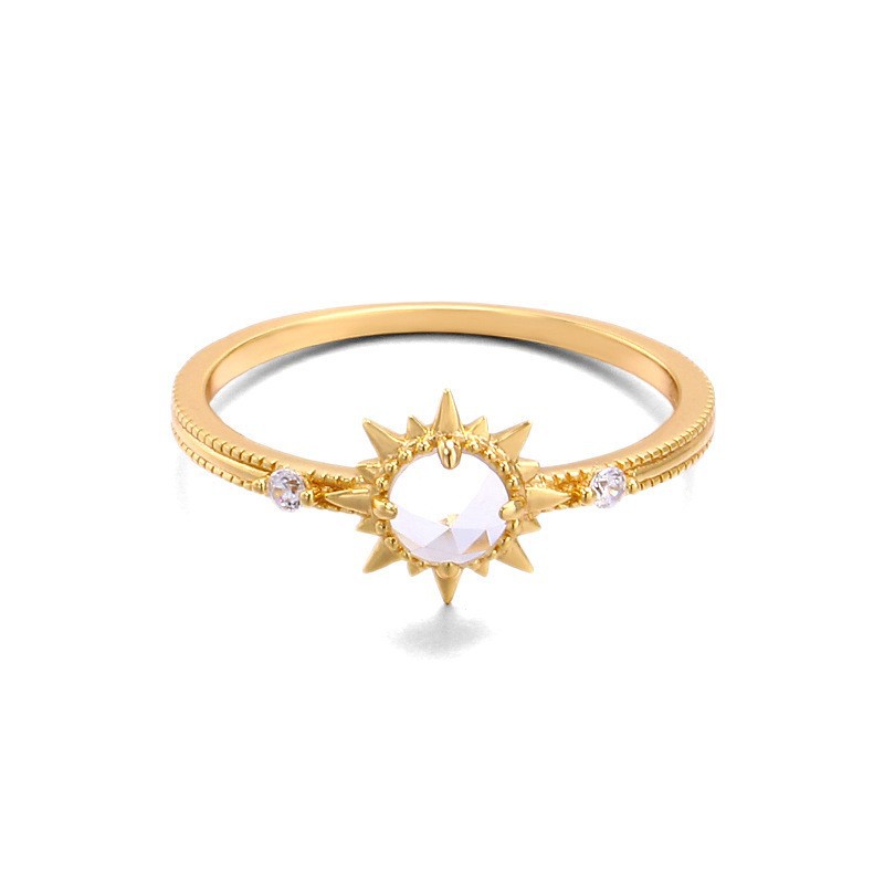 Gold ring with sun design and clear gemstone on a white background