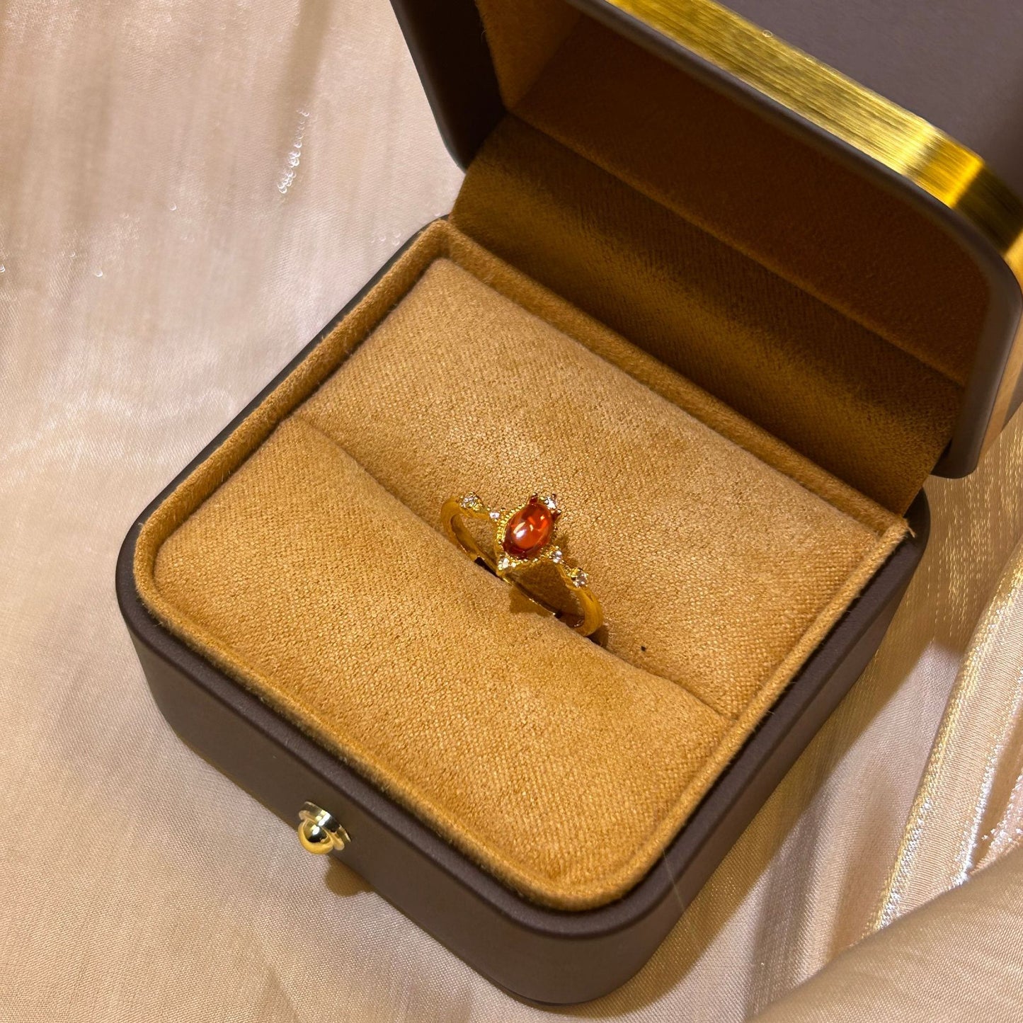 Gold ring with a red gemstone in an open jewelry box on a beige fabric background