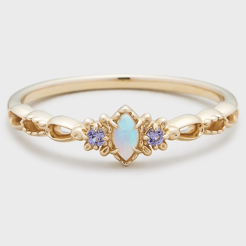 Gold ring with a central opal stone and two smaller purple stones on a light gray background
