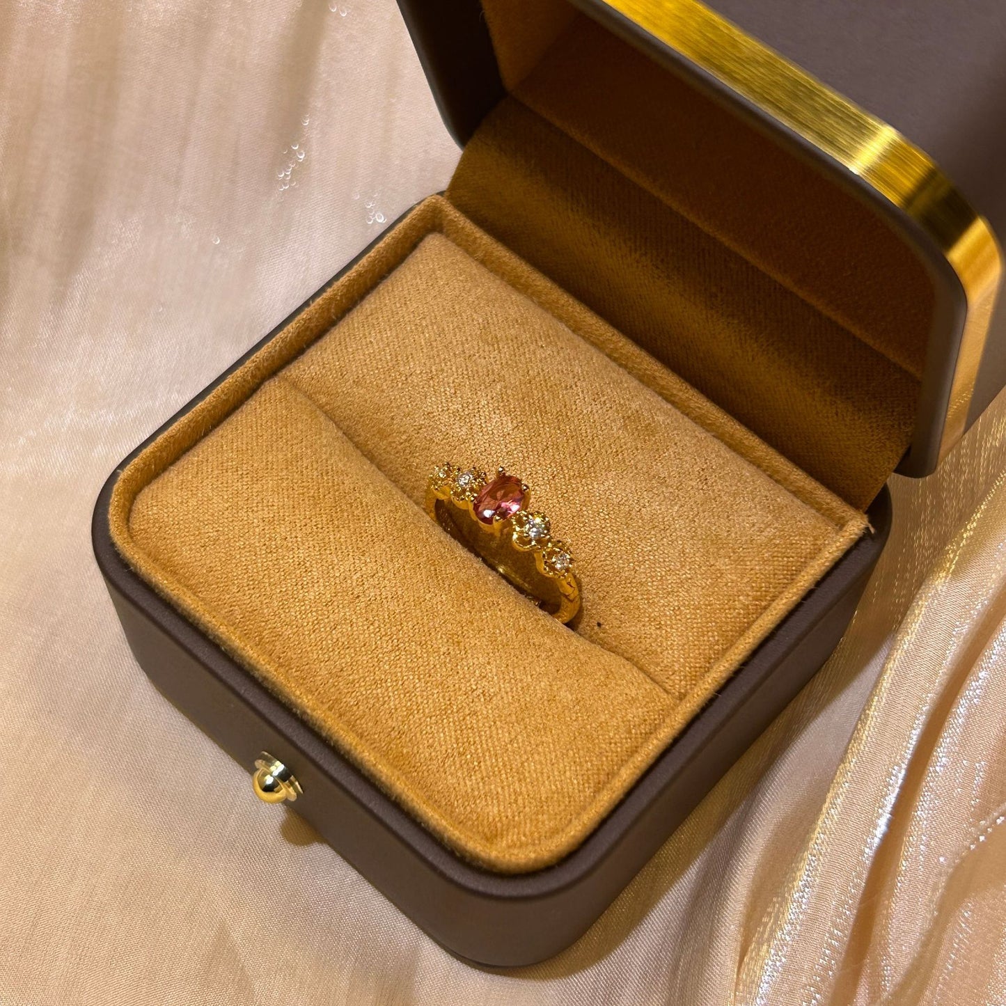 Gold ring with red gemstone in a jewelry box on a beige fabric background