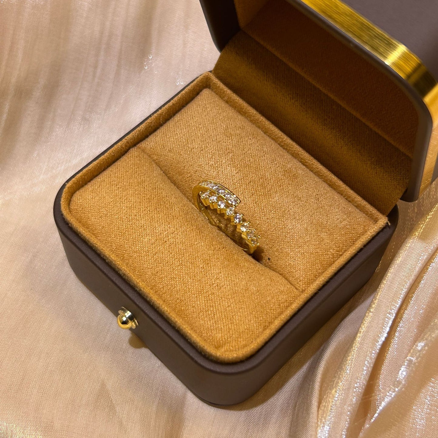 Gold ring with diamonds in a brown jewelry box on a beige fabric background