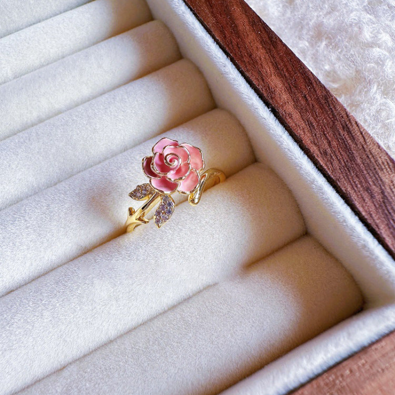 Pink rose ring with gold and gemstone accents on a white jewelry box.