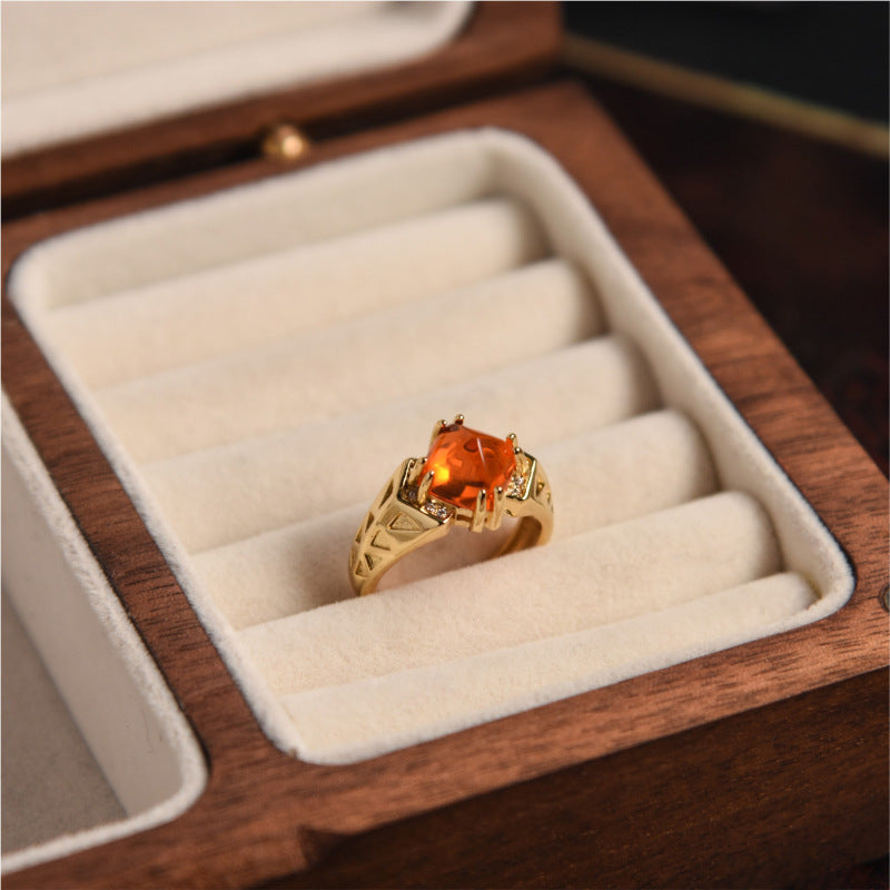 Gold ring with a large orange gemstone in a wooden jewelry box.
