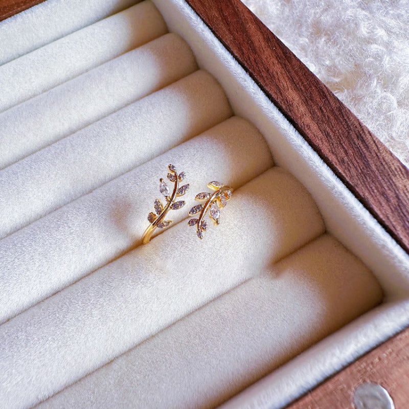 Delicate gold ring with leaf design on a white cushion in a jewelry box.