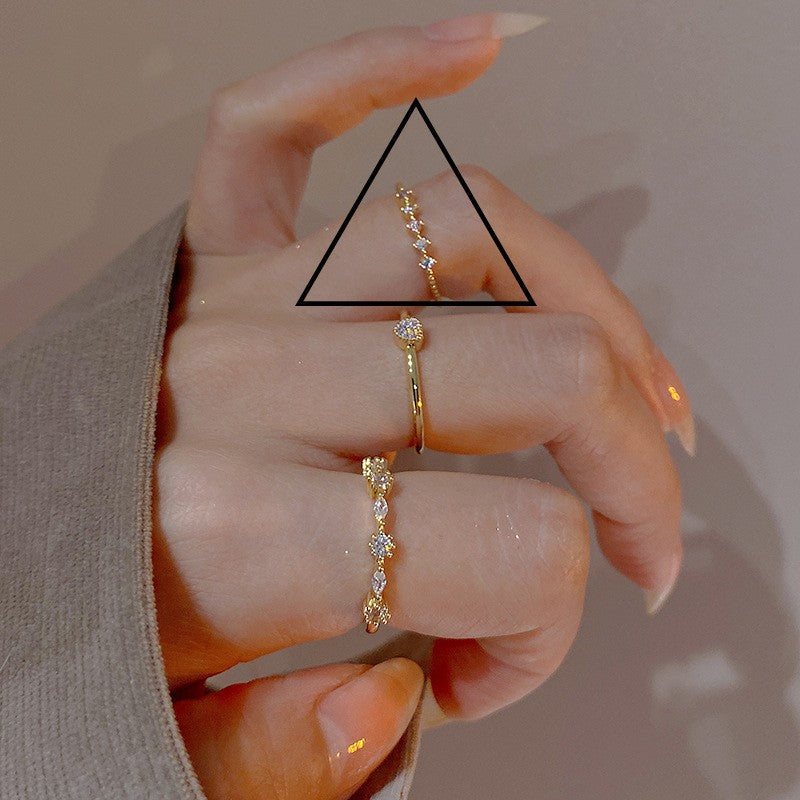 Hand wearing three gold rings with a triangle overlay on a neutral background