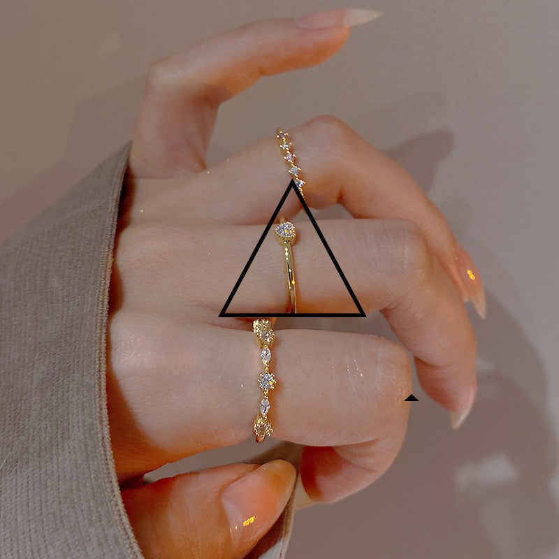 Hand wearing two gold rings with a triangle overlay on a neutral background