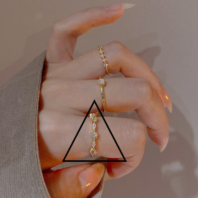 Hand wearing three gold rings with a triangle overlay on a neutral background