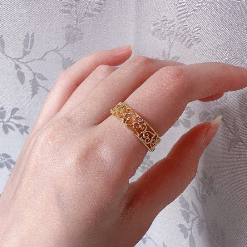 Hand wearing a gold ring with intricate design against a floral background