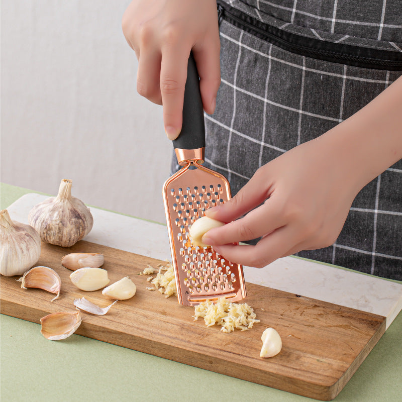Person using a garlic press on garlic cloves on a wooden cutting board.