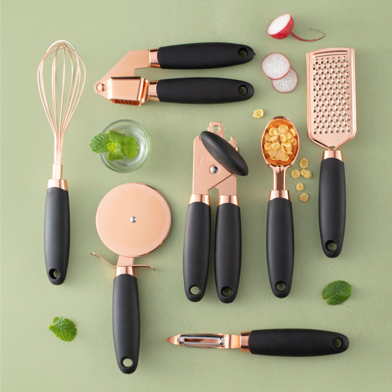 Set of kitchen utensils with rose gold and black handles on a green background