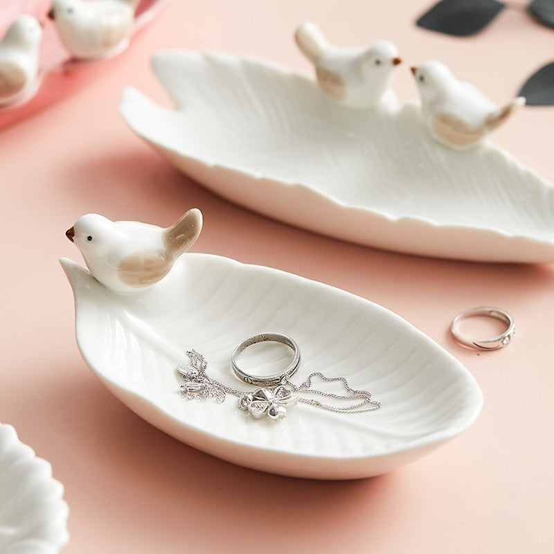 White ceramic dish shaped like a bird with jewelry on a pink surface
