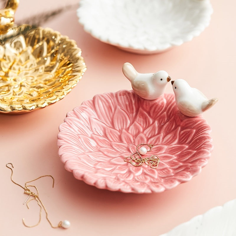 Pink jewelry dish with two ceramic birds and a gold earring on a pink background