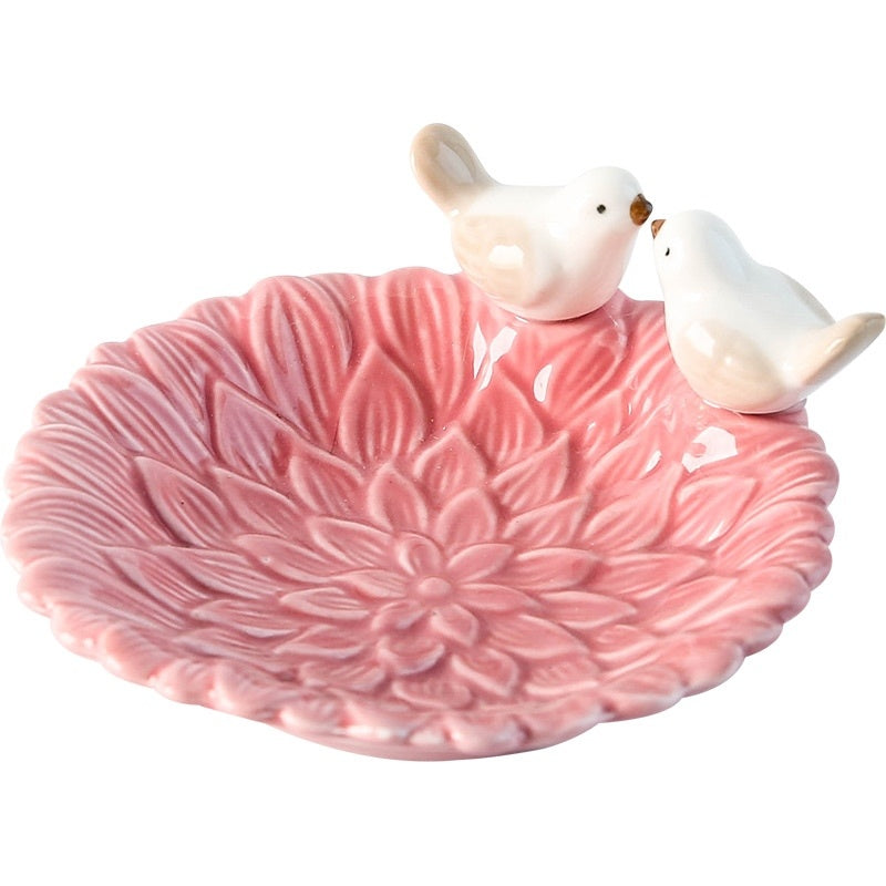 Pink ceramic dish with floral patterns and two small bird figurines on a white background