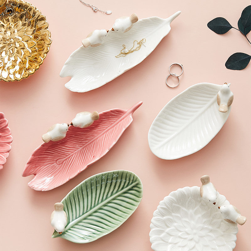 Set of leaf-shaped ceramic dishes with animal figurines on a pink background