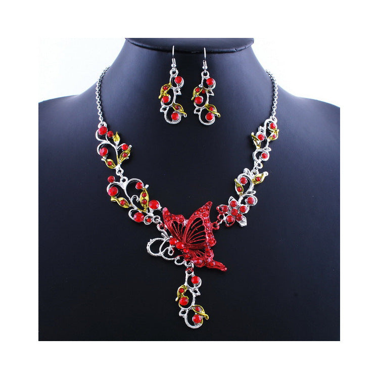 Jewelry set with a necklace and earrings featuring red and gold butterfly design on a black mannequin.