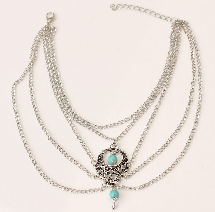 Stack of layered necklaces with a central pendant featuring turquoise stones on a light background