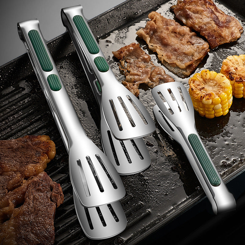 Set of four silver and green grilling utensils on a grill with meat and corn.