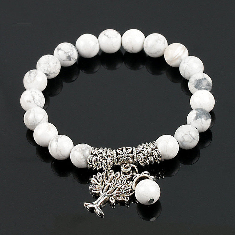 White beaded bracelet with silver tree charm on a black background