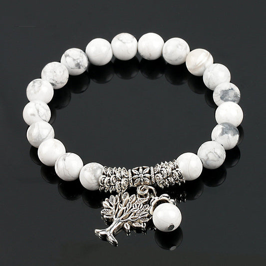 White beaded bracelet with silver tree charm on a black background